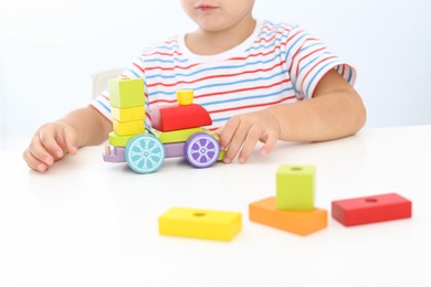 Photo of Little boy playing with toy at white table, closeup