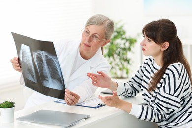 Lung disease. Doctor showing chest x-ray to her patient at table in clinic