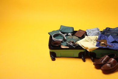 Photo of Open suitcase with traveler's belongings on yellow background, space for text