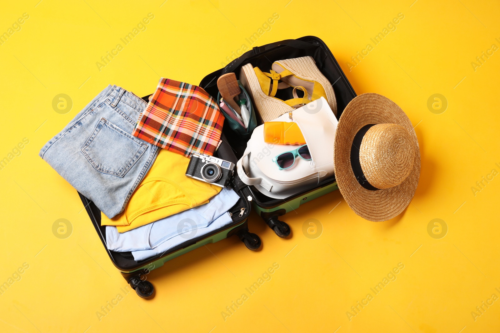 Photo of Open suitcase with traveler's belongings on yellow background, top view