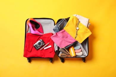 Photo of Open suitcase with traveler's belongings on yellow background, top view