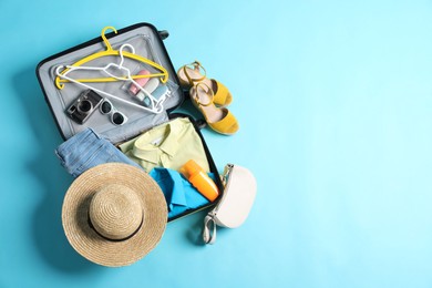 Open suitcase with traveler's belongings on light blue background, flat lay. Space for text