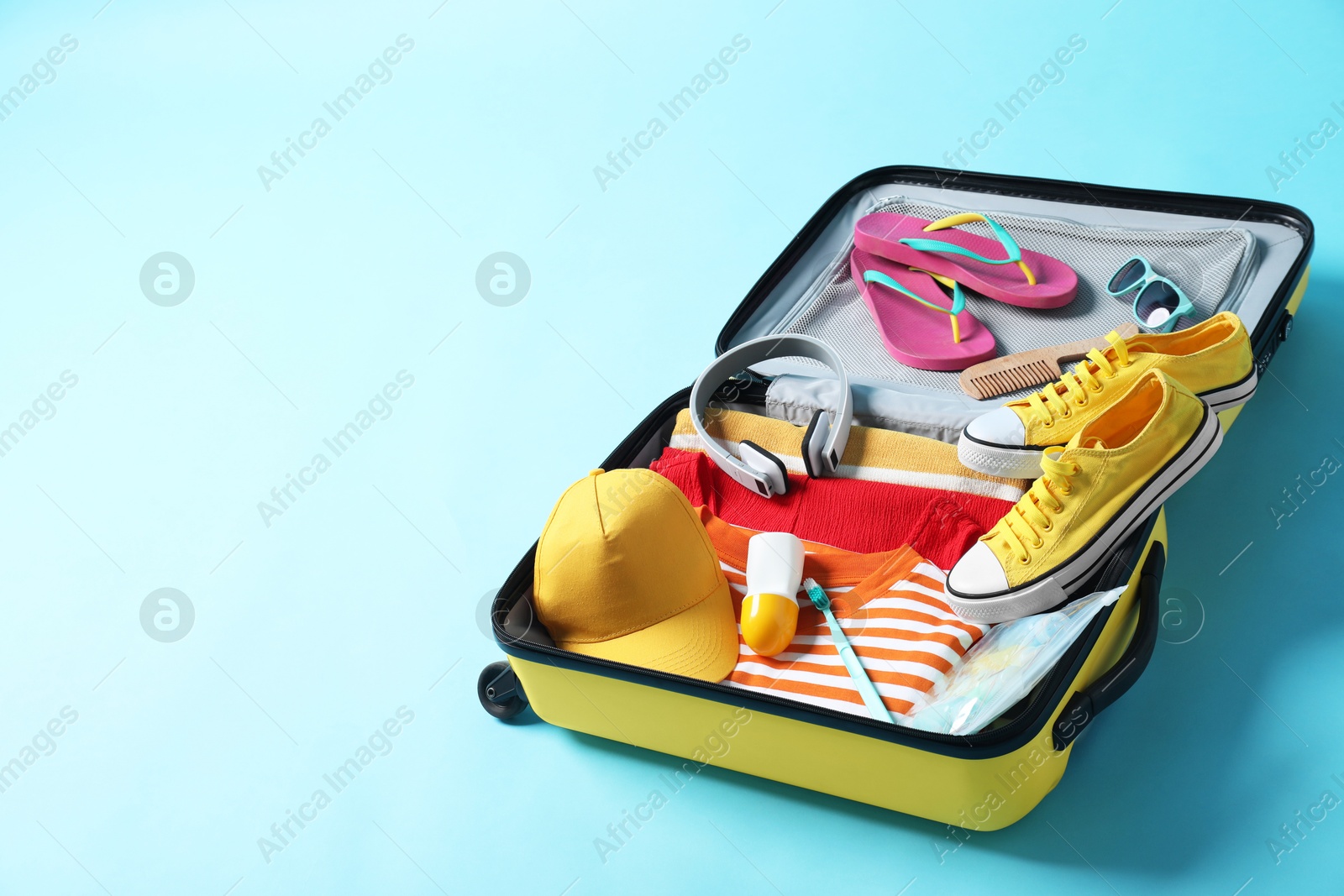 Photo of Open suitcase with traveler's belongings on light blue background, space for text