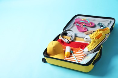 Open suitcase with traveler's belongings on light blue background, space for text