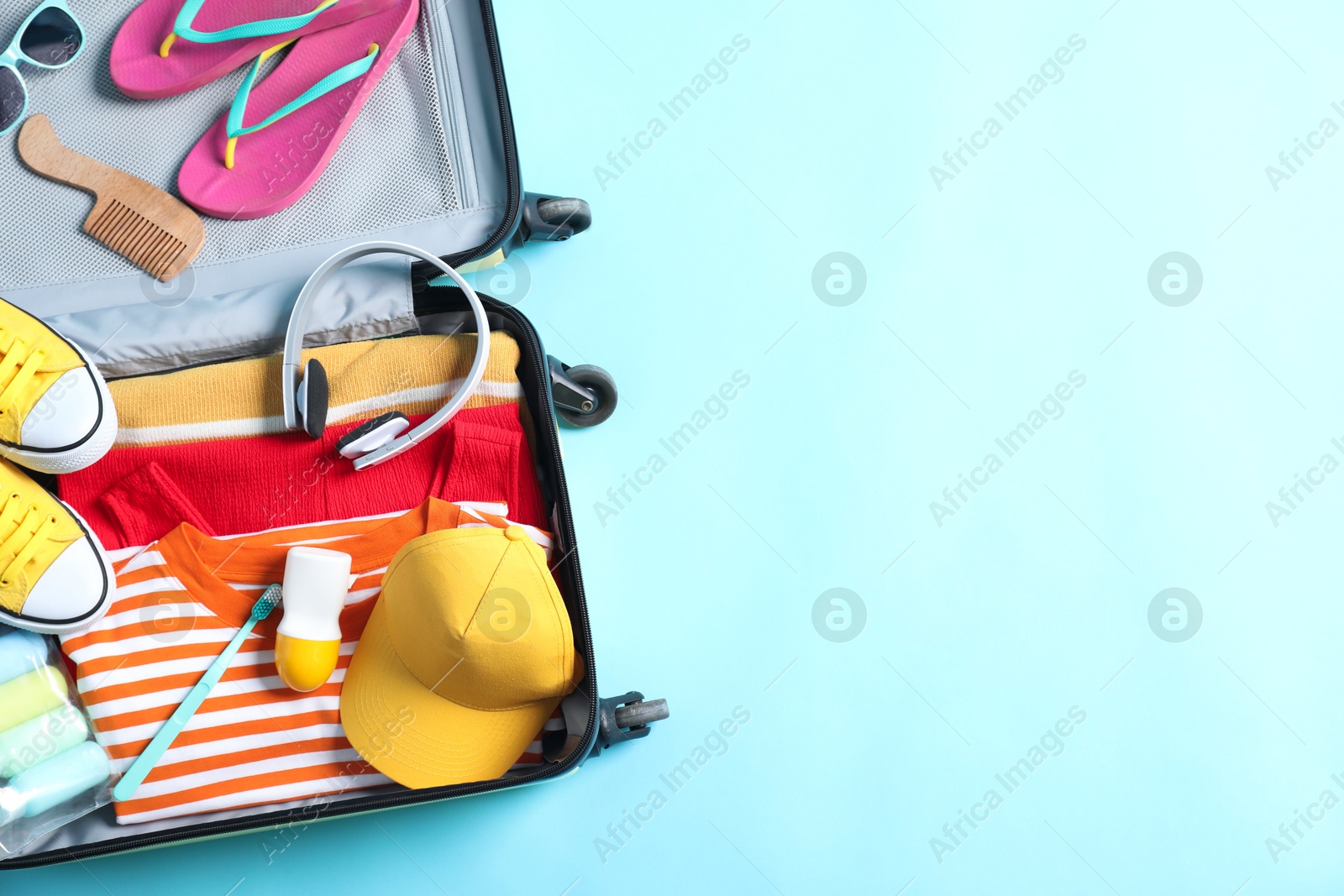 Photo of Open suitcase with traveler's belongings on light blue background, top view. Space for text