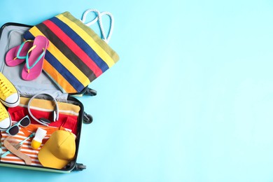 Open suitcase with traveler's belongings on light blue background, top view. Space for text