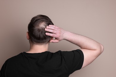 Photo of Baldness concept. Man with bald spot on beige background, back view