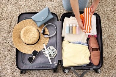 Photo of Woman packing suitcase for trip on floor indoors, top view