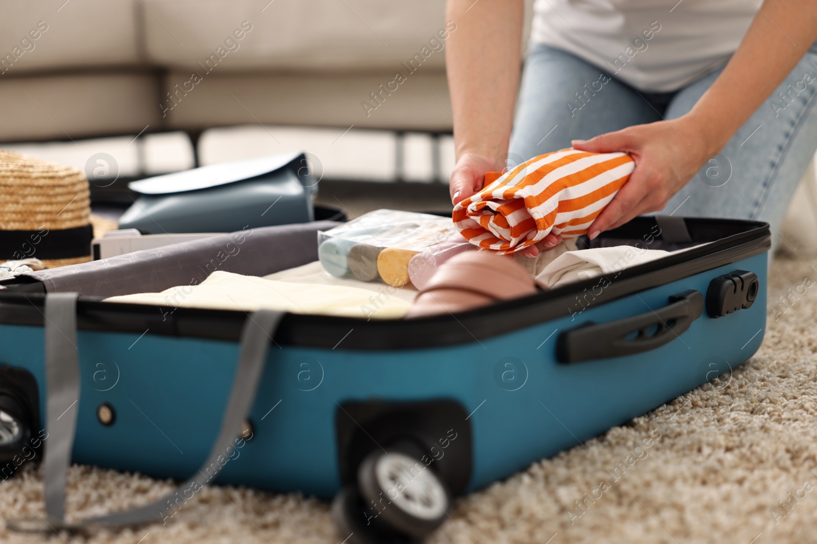 Photo of Woman packing suitcase for trip on floor indoors, closeup