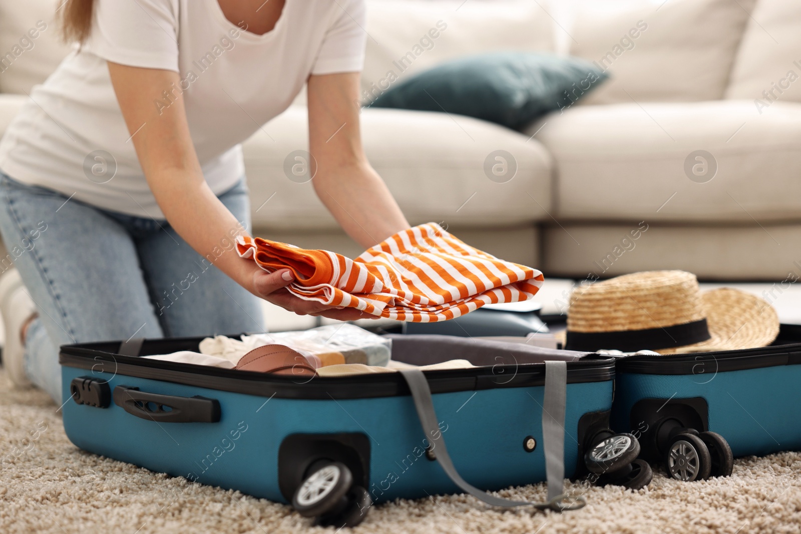 Photo of Woman packing suitcase for trip on floor indoors, closeup