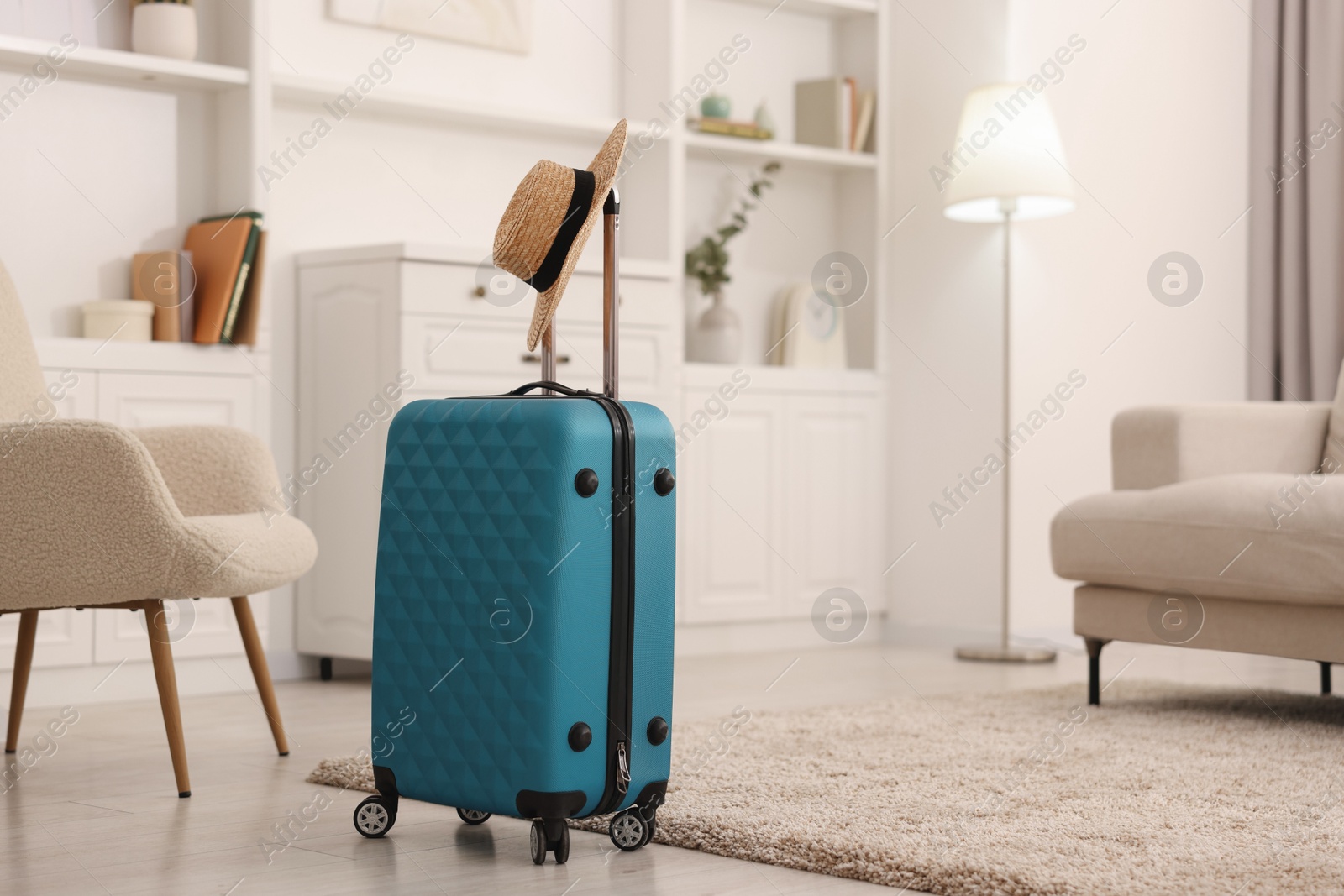 Photo of Light blue suitcase and straw hat indoors