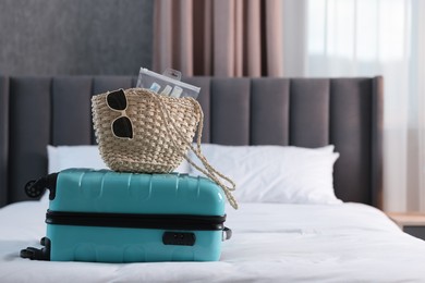 Turquoise suitcase, bag, sunglasses and cosmetic travel kit on bed indoors