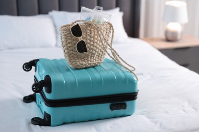 Turquoise suitcase, bag, sunglasses and cosmetic travel kit on bed indoors