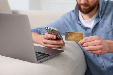 Photo of Online banking. Man with credit card and laptop paying purchase at home, selective focus