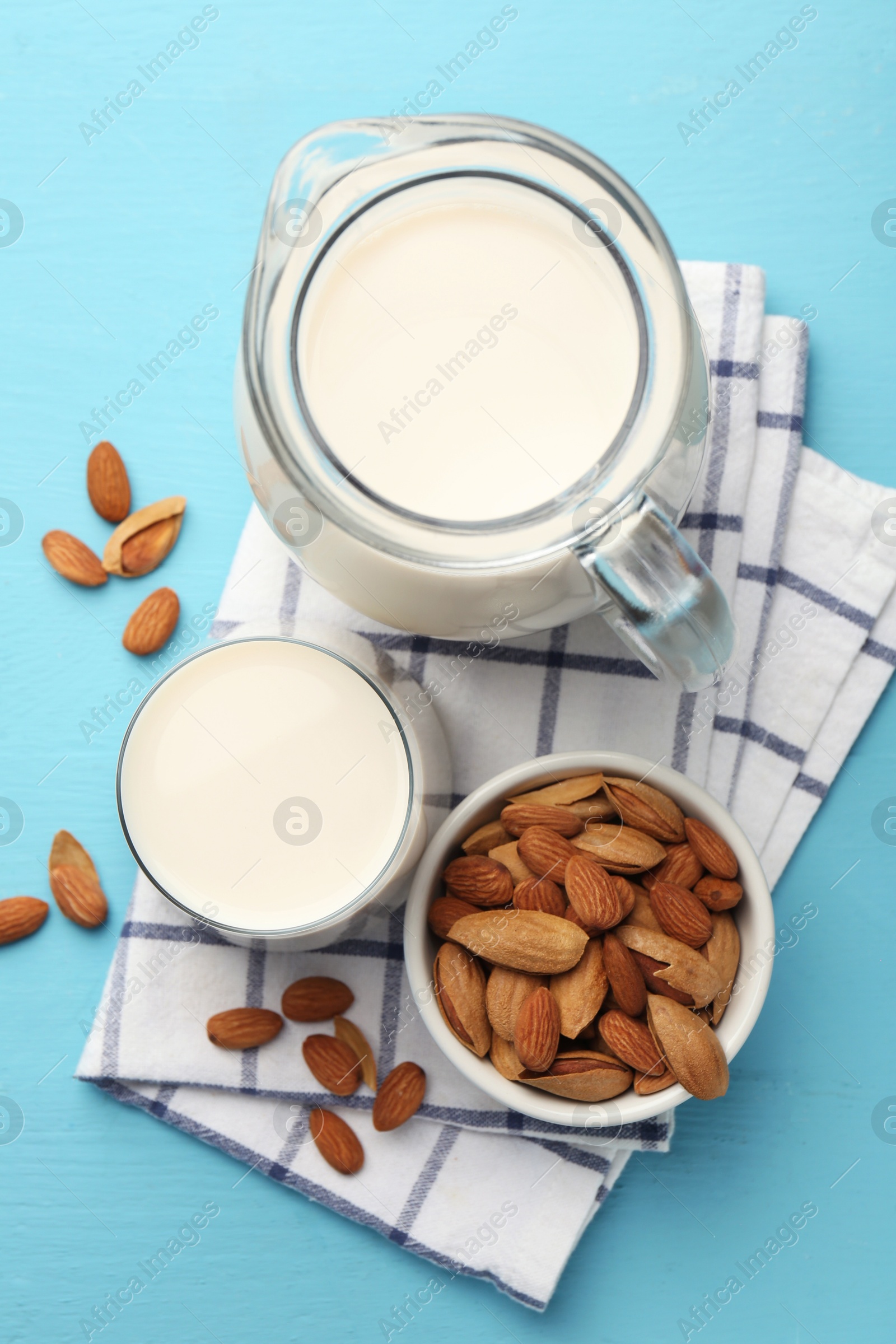 Photo of Glass of almond milk, jug and almonds on light blue wooden table, top view