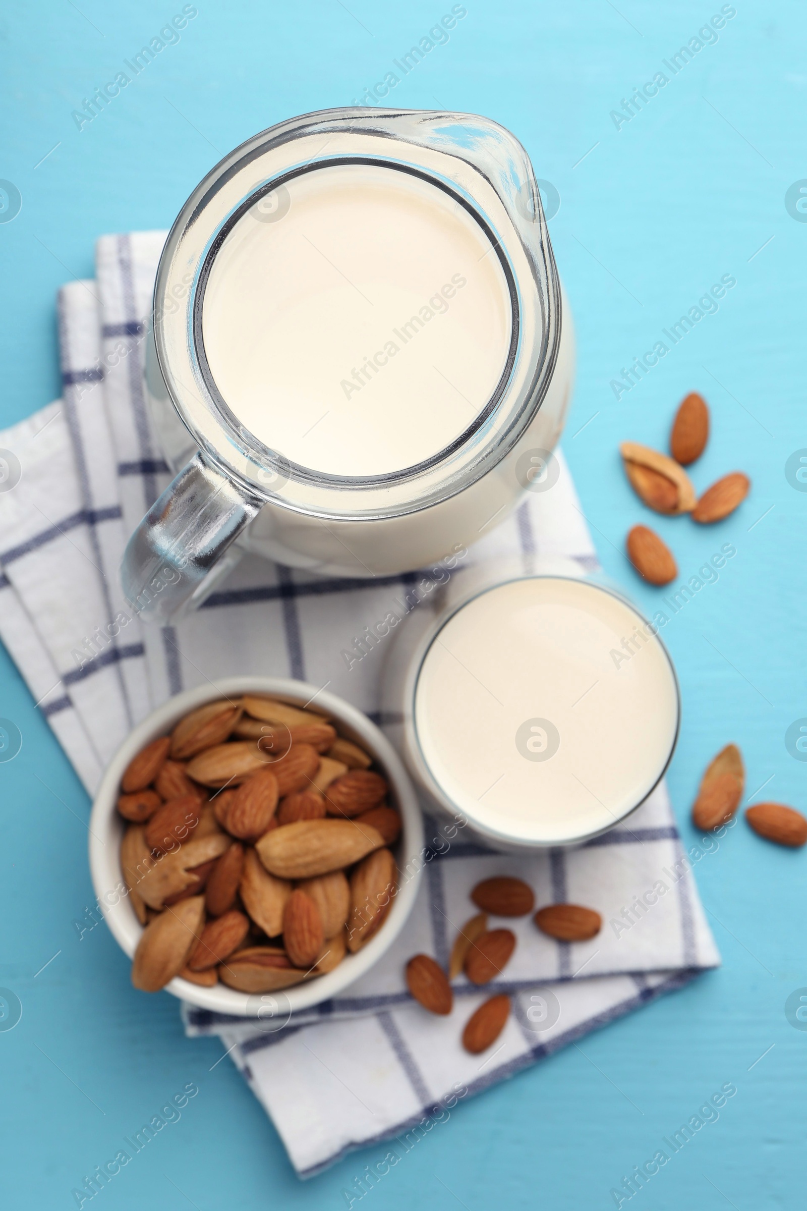 Photo of Glass of almond milk, jug and almonds on light blue wooden table, top view