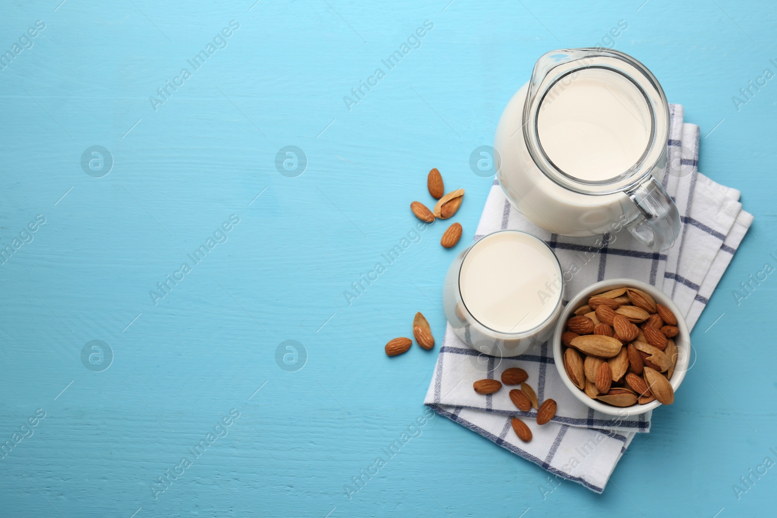 Photo of Glass of almond milk, jug and almonds on light blue wooden table, top view. Space for text