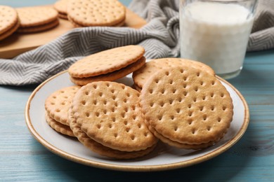 Photo of Tasty sandwich cookies and glass of milk on light blue wooden table, closeup