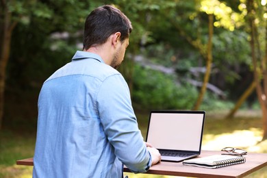 Freelancer working with laptop at table in forest, back view. Remote job