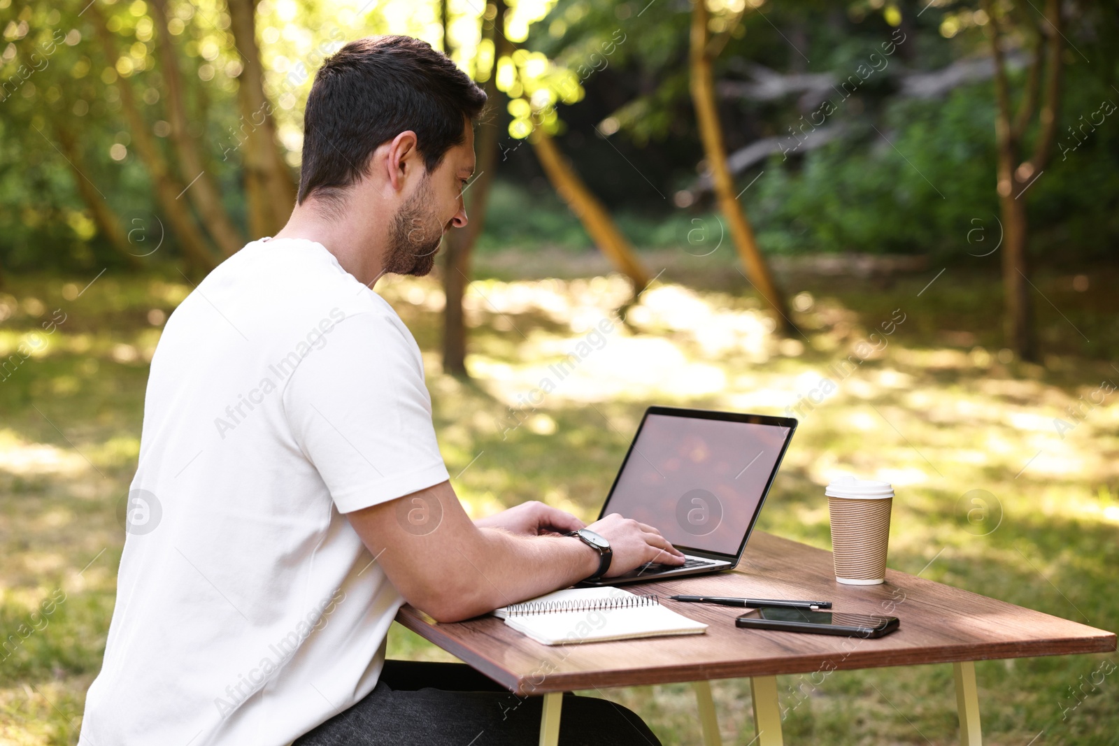 Photo of Freelancer working with laptop at table outdoors on sunny day. Remote job