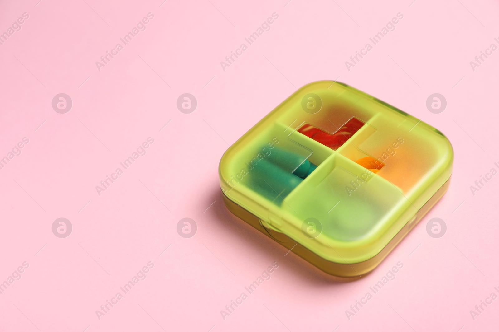 Photo of Different pills in organizer on pink background, space for text