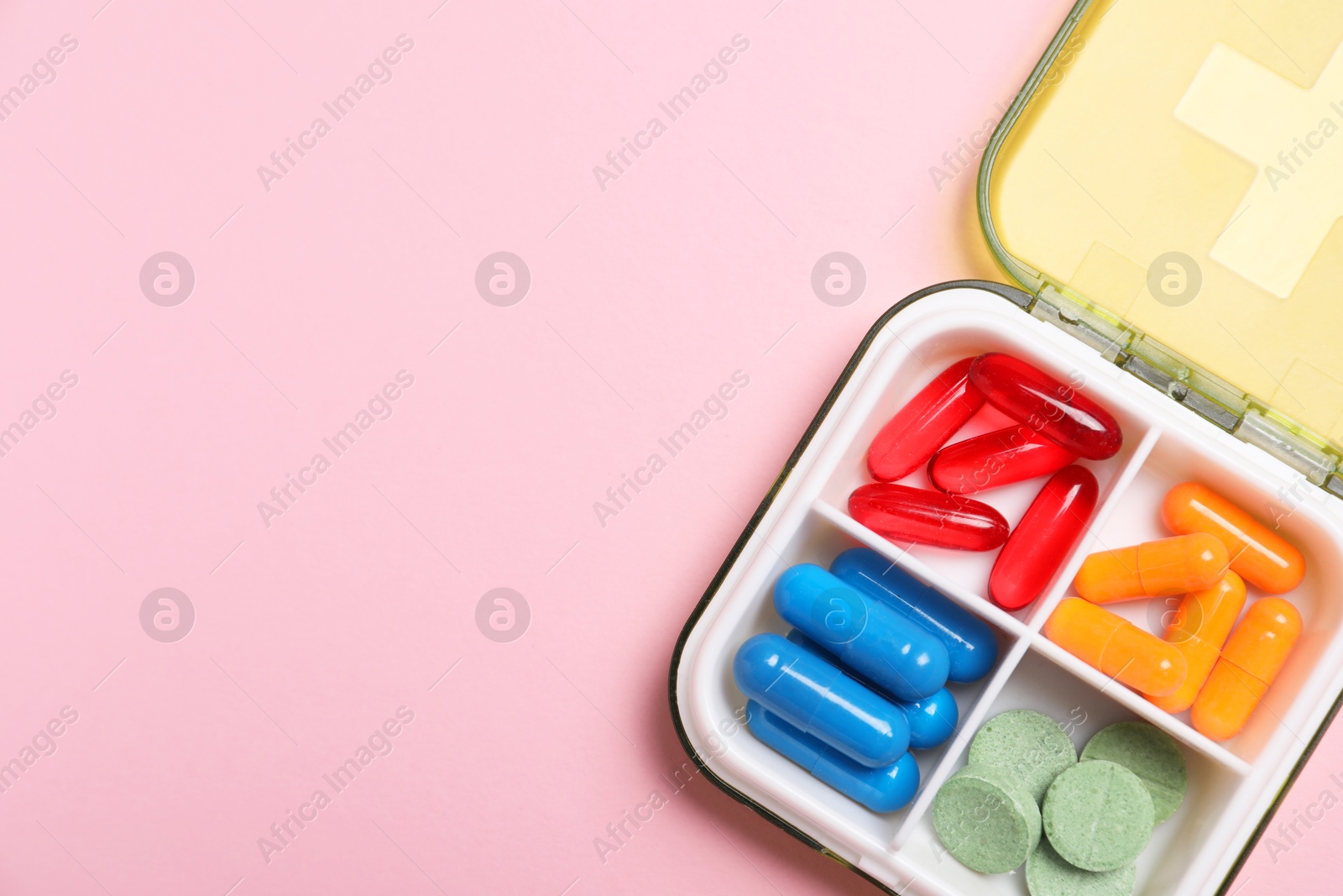 Photo of Different pills in organizer on pink background, top view. Space for text