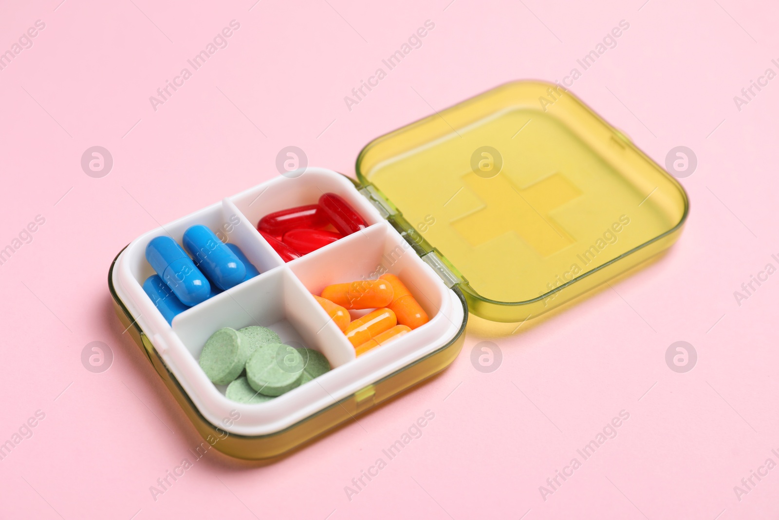 Photo of Different pills in organizer on pink background, closeup