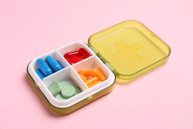 Photo of Different pills in organizer on pink background, closeup