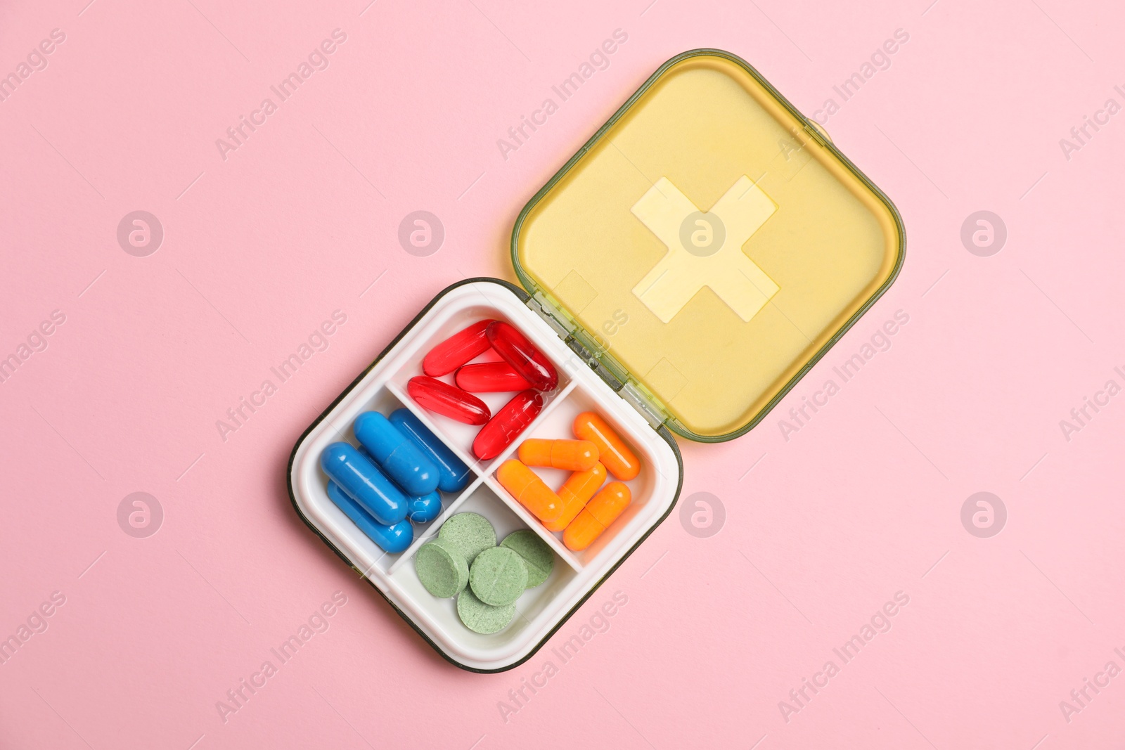 Photo of Different pills in organizer on pink background, top view