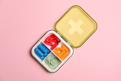 Photo of Different pills in organizer on pink background, top view