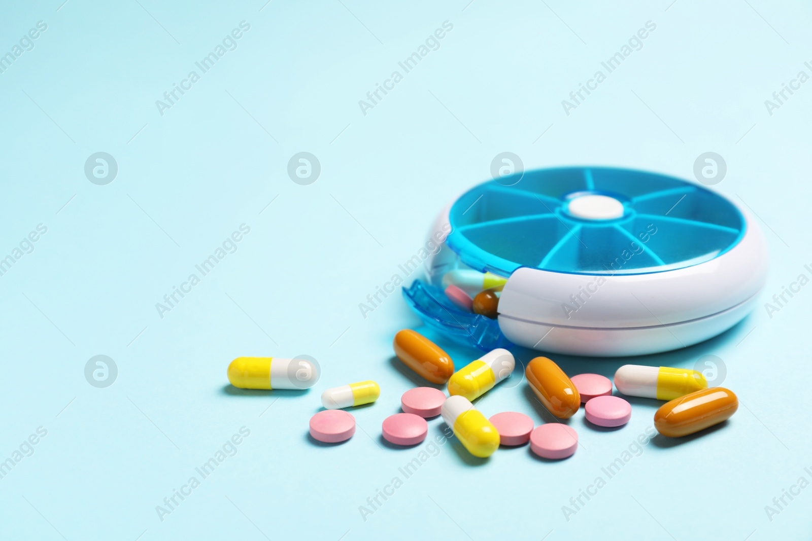 Photo of Different pills and organizer on light blue background, space for text