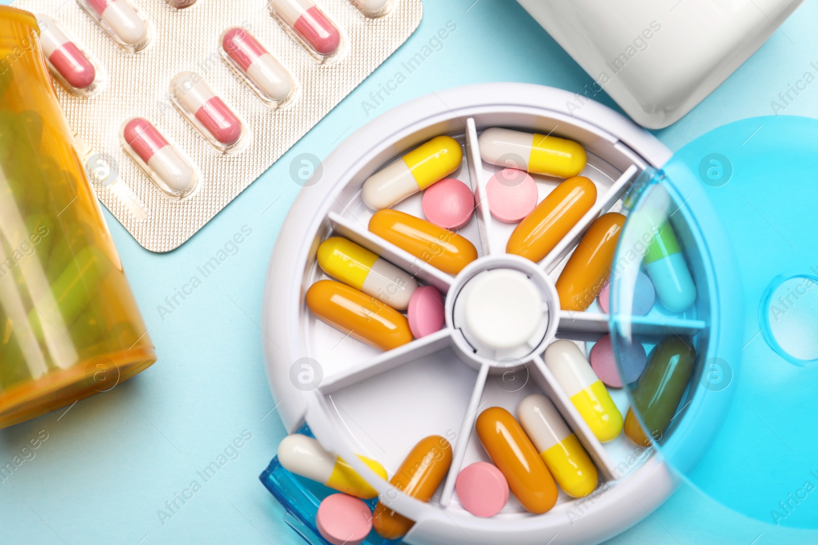 Photo of Pills, organizer and medical jars on light blue background, flat lay