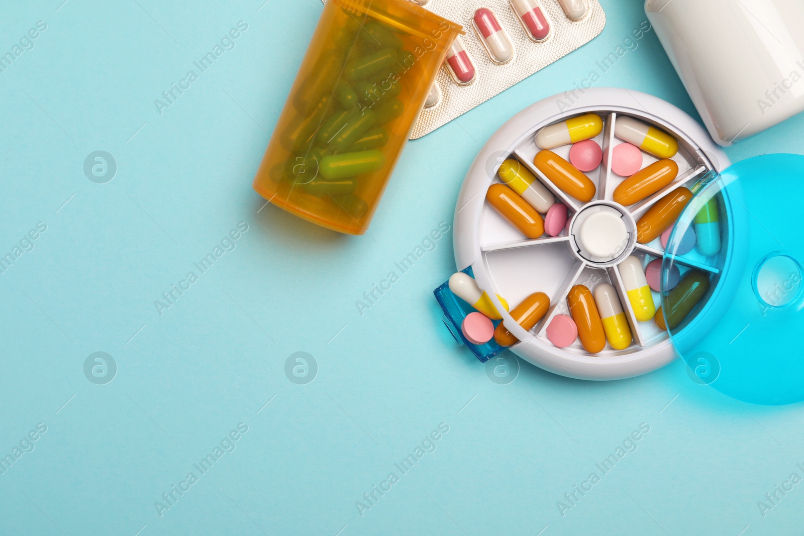 Photo of Pills, organizer and medical jars on light blue background, flat lay. Space for text