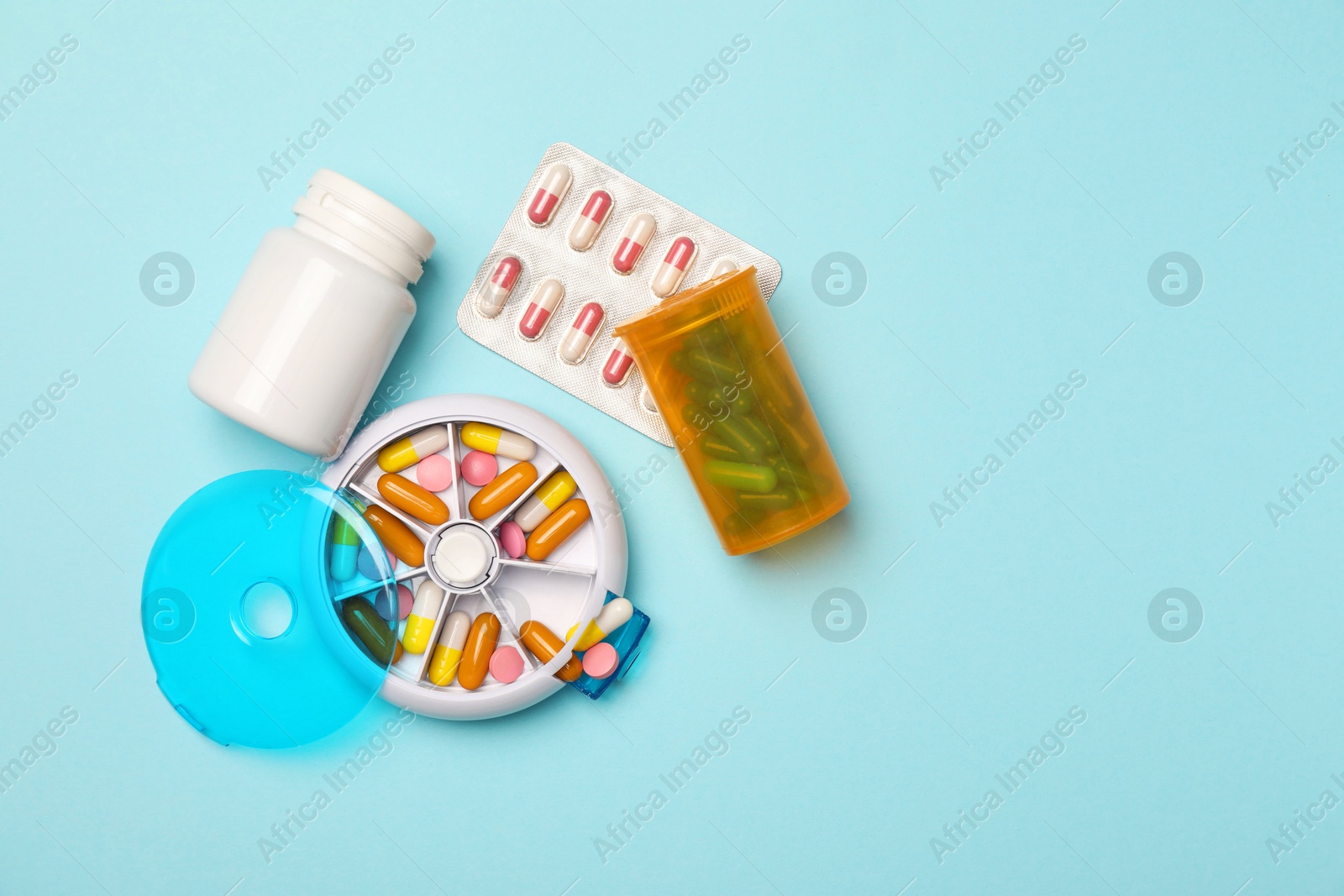 Photo of Pills, organizer and medical jars on light blue background, flat lay. Space for text