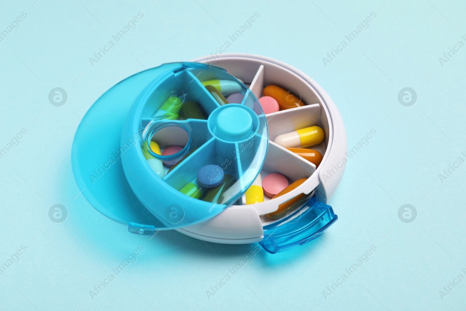 Photo of Different pills in organizer on light blue background