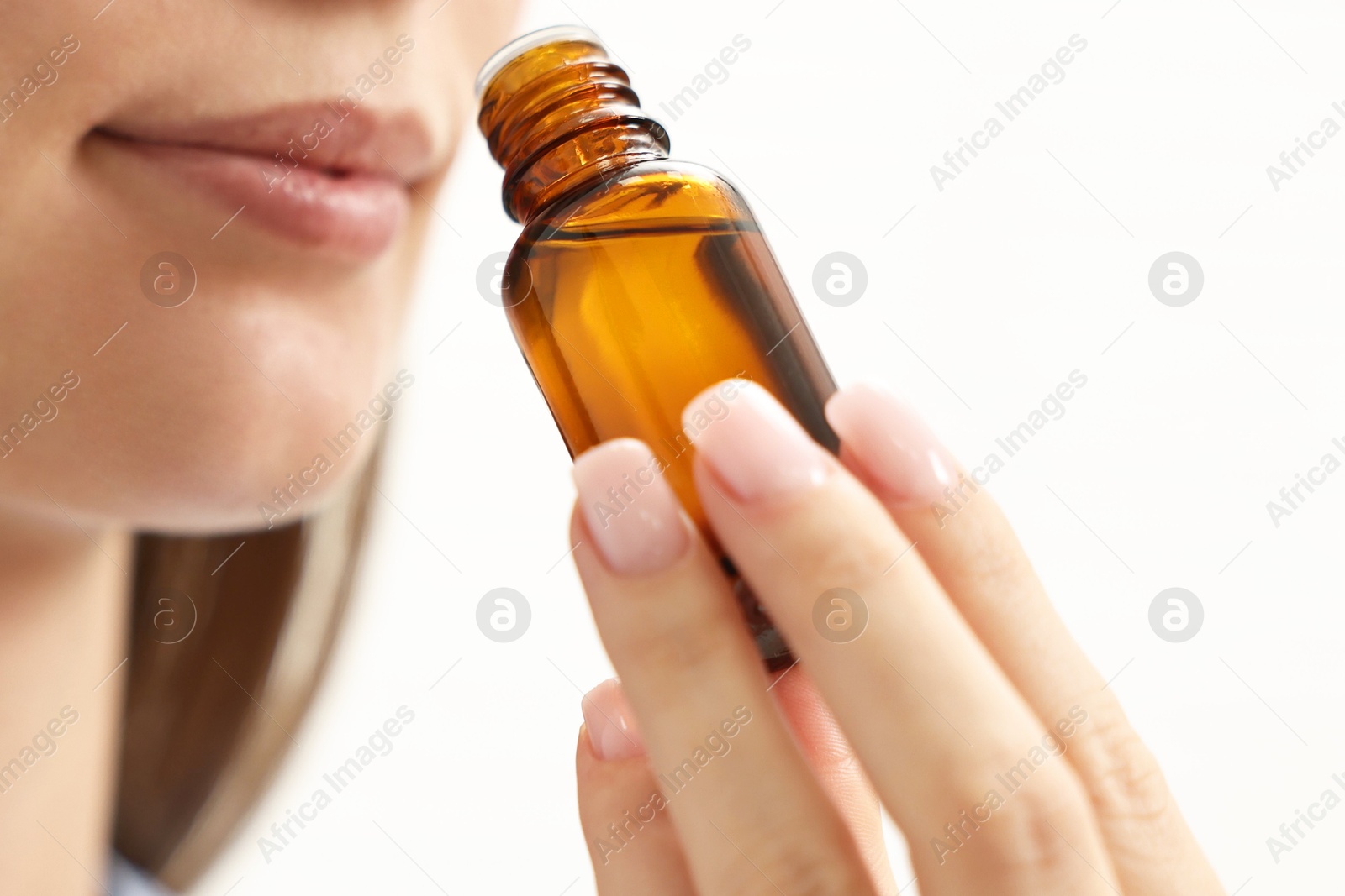 Photo of Aromatherapy. Woman with bottle of essential oil on light background, closeup