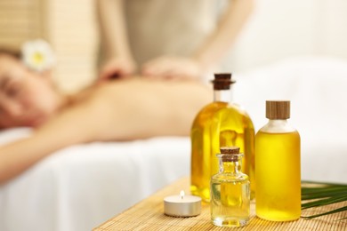 Aromatherapy. Woman receiving back massage in spa salon, focus on bottles of essential oils and burning candle