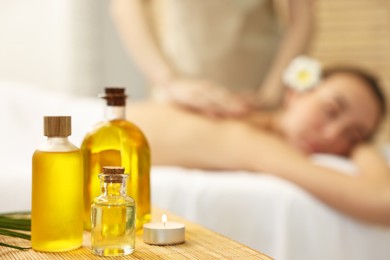 Aromatherapy. Woman receiving back massage in spa salon, focus on bottles of essential oils and burning candle