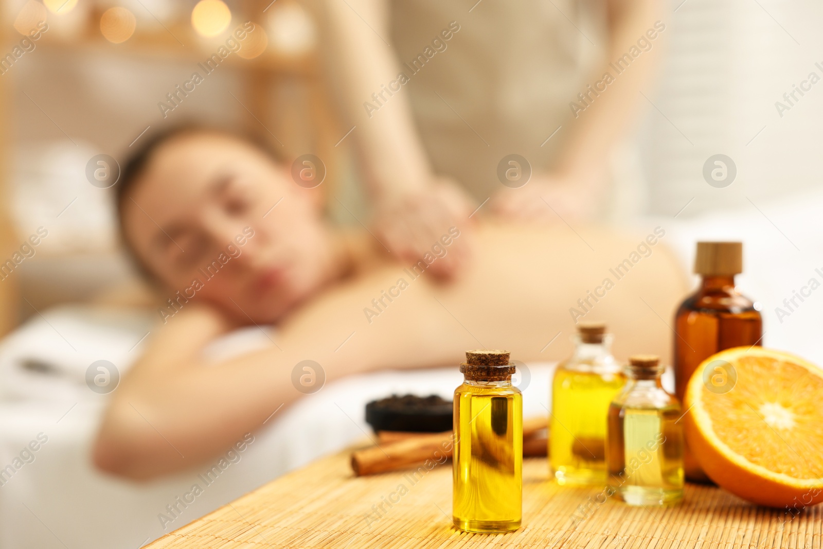 Photo of Aromatherapy. Woman receiving back massage in spa salon, focus on bottles of essential oils