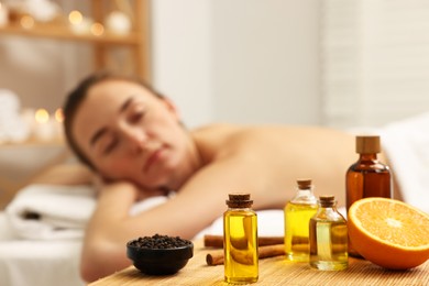 Aromatherapy. Woman relaxing on massage couch in spa salon, focus on table with bottles of essential oils and other aromatic products