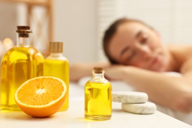 Photo of Aromatherapy. Woman relaxing on massage couch in spa salon, focus on bottles of essential oils, orange and stones