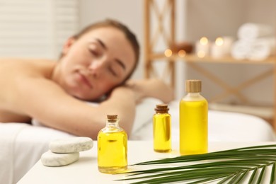 Aromatherapy. Woman relaxing on massage couch in spa salon, focus on bottles of essential oils, stones and palm leaf