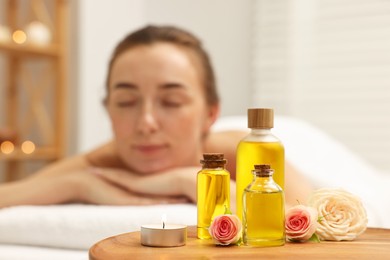 Aromatherapy. Woman relaxing on massage couch in spa salon, focus on bottles of essential oils, burning candle and rose flowers