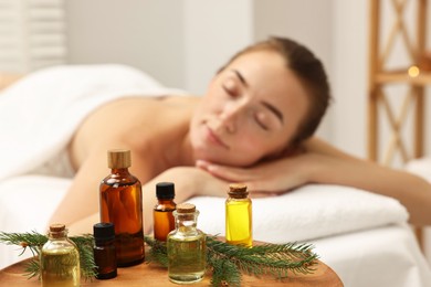 Aromatherapy. Woman relaxing on massage couch in spa salon, focus on bottles of essential oils and fir branch