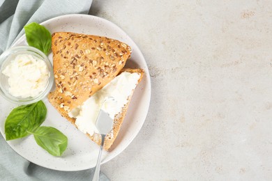 Photo of Pieces of bread with cream cheese and basil leaves on light gray textured table, top view. Space for text