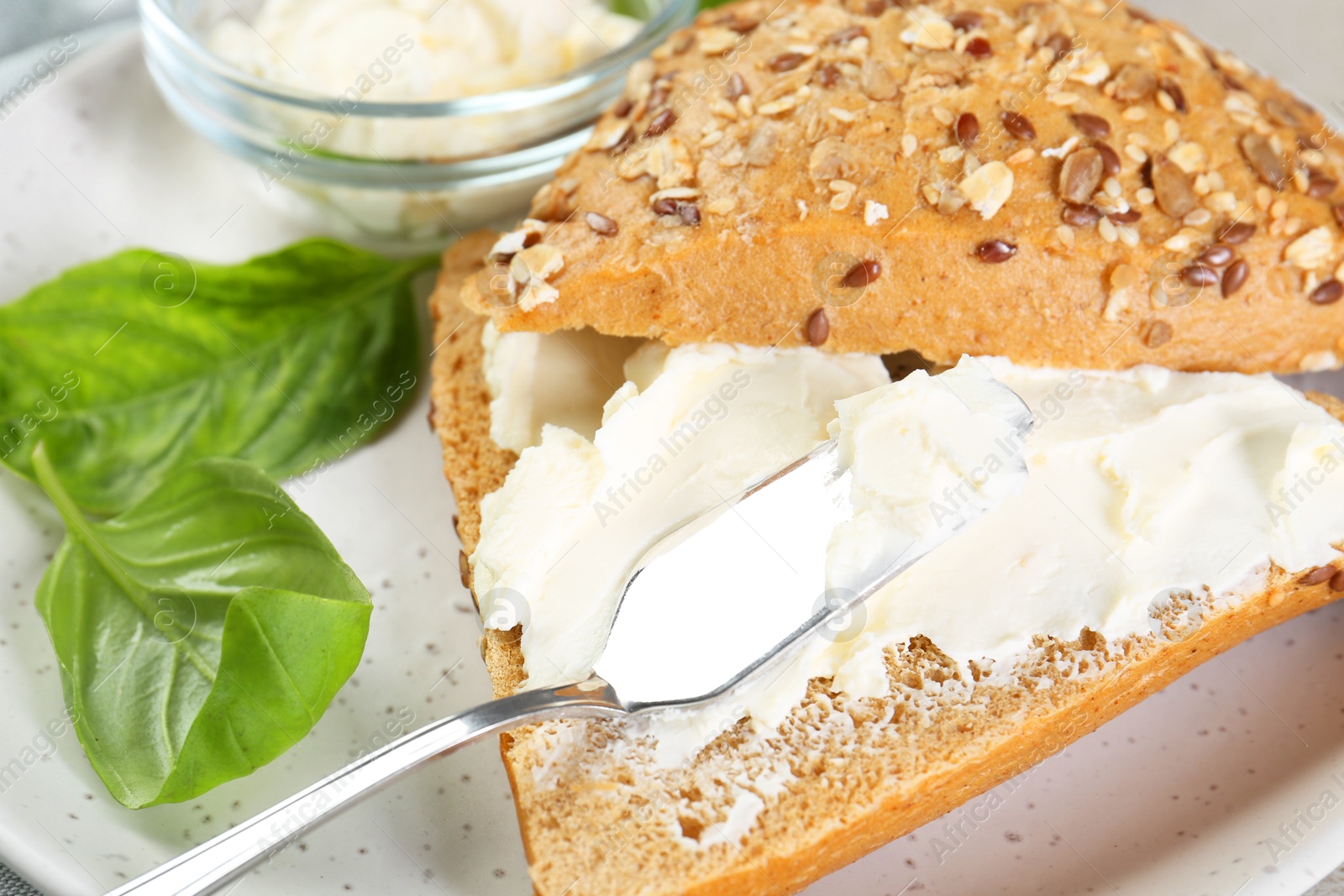 Photo of Pieces of bread with cream cheese and basil leaves on plate, closeup