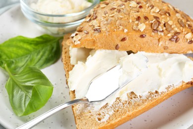 Pieces of bread with cream cheese and basil leaves on plate, closeup