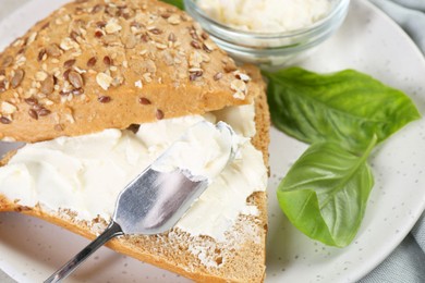 Pieces of bread with cream cheese and basil leaves on plate, closeup