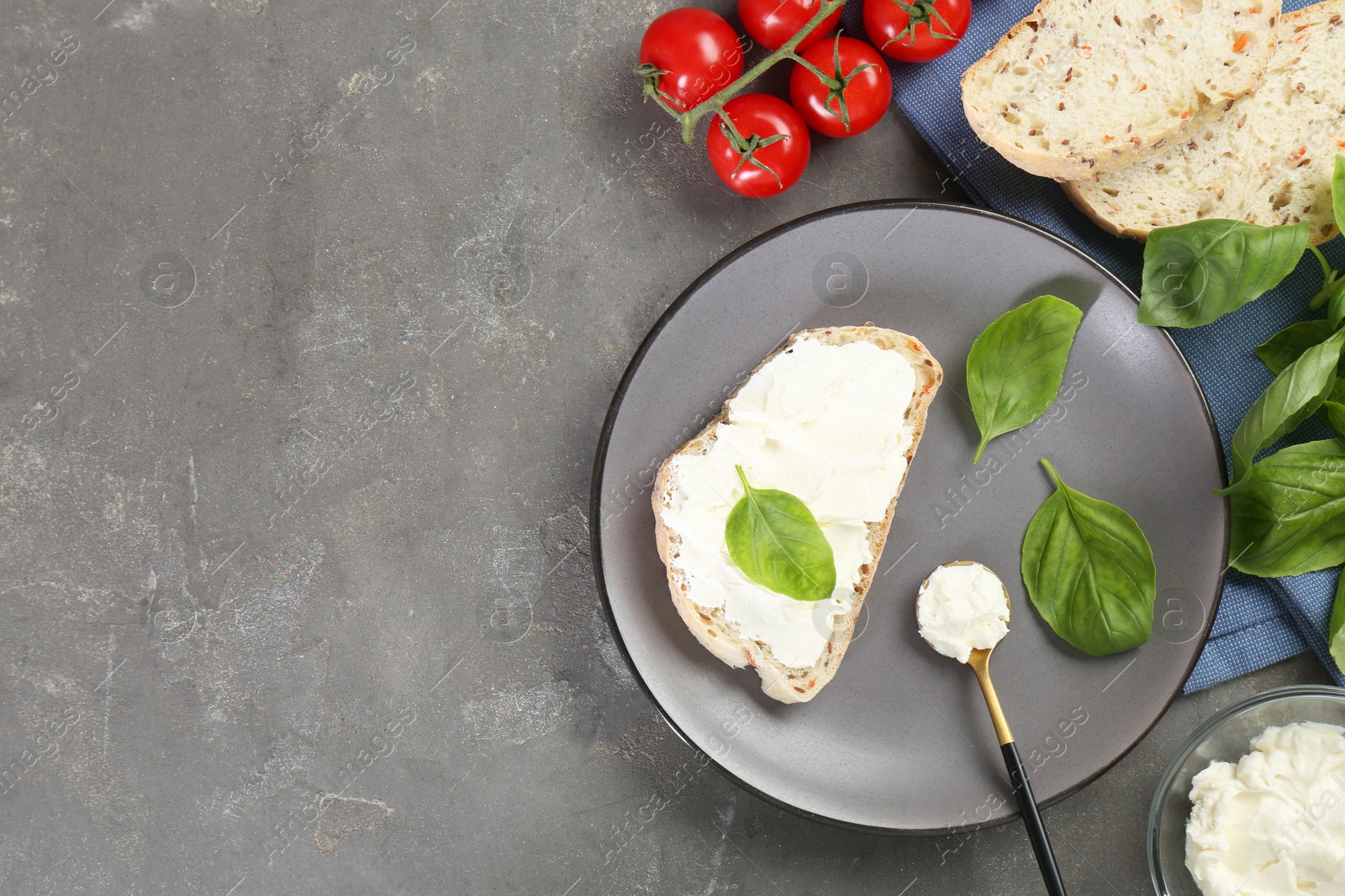 Photo of Pieces of bread with cream cheese, basil leaves and tomatoes on gray textured table, flat lay. Space for text