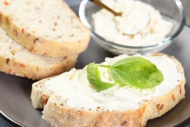 Photo of Pieces of bread with cream cheese and basil leaves on gray plate, closeup